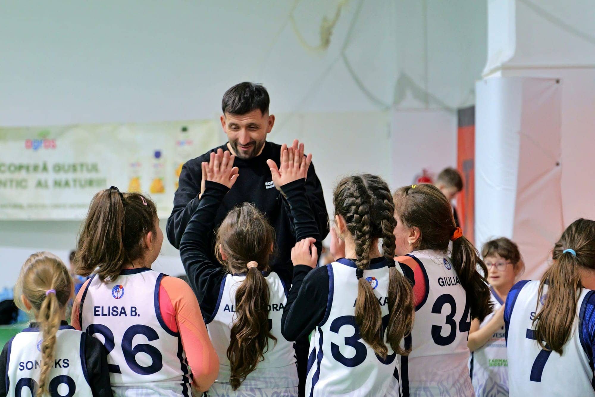 Erkek antrenör kapalı salonda forma giymiş kız basketbolcularla el çakıyor